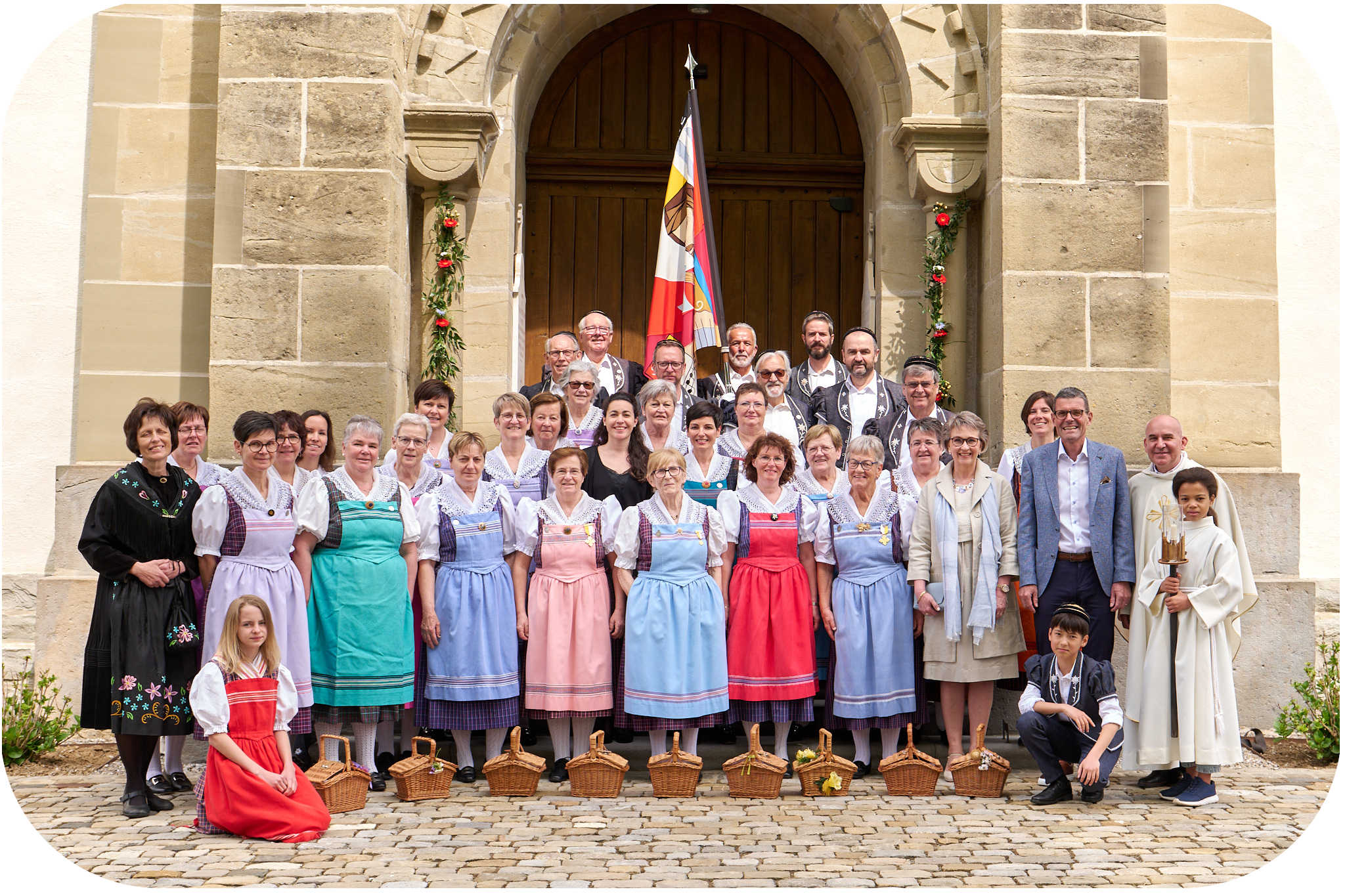 On voit le chœur mixte de Rossens en costume d'époque, posant devant l'église de Rossens à l'occasion de la célébration de la nouvelle bannière en 2023